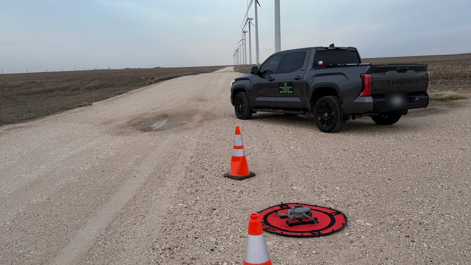 Drone Force truck, safety cones and an inspection drone on its landing pad on a wind farm access road